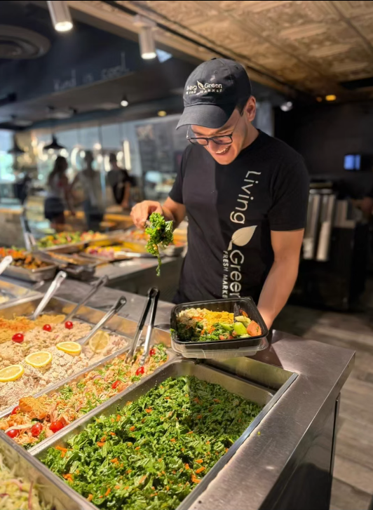 Living Green Cafe team member plating fresh salad and hot bar items into a to-go container